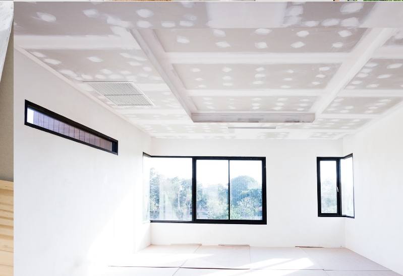 A freshly taped and mudded room with a finished ceiling grid and daylight through the windows